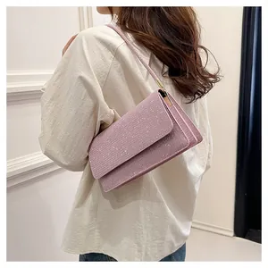 Side view of a pink rhinestone shoulder bag worn by a model against a white wall