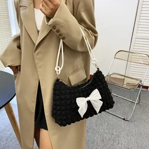 Detail view of black waffle texture shoulder bag featuring a large white bow and rope strap