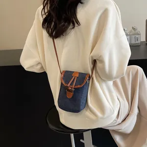 Denim crossbody phone bag with brown leather trim and toggle closure on model