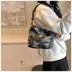 Detail of grey shoulder bag with silver butterfly embroidery and beaded braided strap