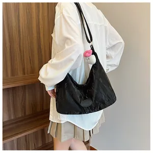 Detail of black pleated shoulder bag with a plush doll charm on model showing size
