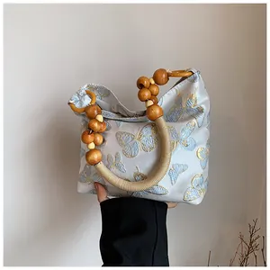Detail of light blue floral jacquard handbag with wooden bead handle and butterfly patterns
