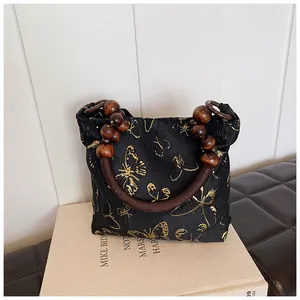 Detailed shot of black brocade tote bag with golden butterfly embroidery and wood bead handle