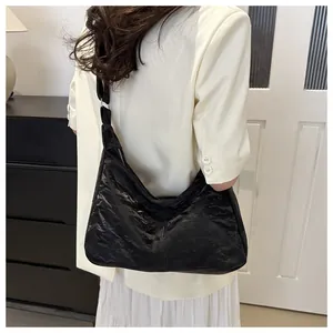 Model shot of a black pleated textured tote bag with a crescent shape and metal zipper