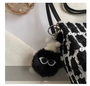 Close-up of cute black plush charm with knit hat and sunglasses on tweed bucket bag