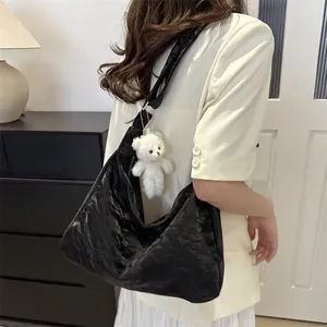 Large black pleated leather tote bag with plush bear pendant shown on shoulder
