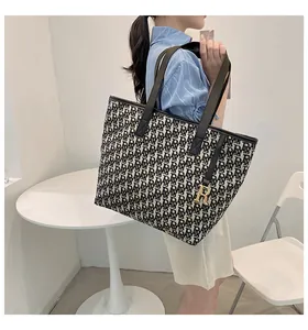 Gros plan du sac cabas en toile avec monogramme noir et breloque dorée en forme de R