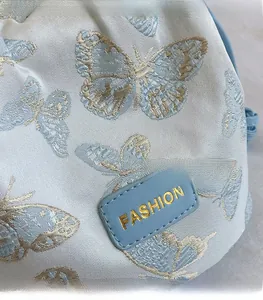 Détail d'un sac en tissu bleu clair avec broderie papillon dorée et logo de mode