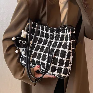 Detail of checkered woven tote bag with black leather straps and plush cartoon charm