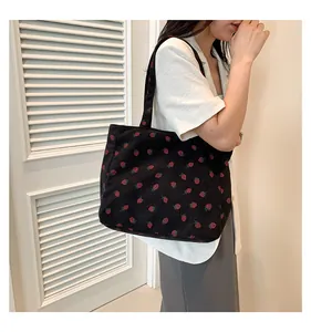 Gros plan d'un sac cabas en velours côtelé noir avec broderie fraise rouge et texture côtelée