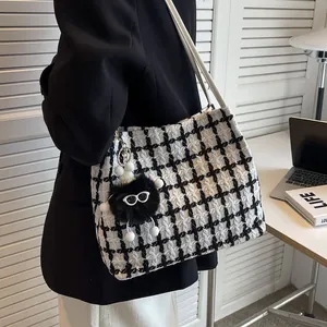 Detail of tweed tote bag with plush charm on shoulder in a modern office setting