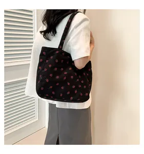 Détail d'un grand sac cabas en velours côtelé noir avec imprimé fraises rouges et bandoulière