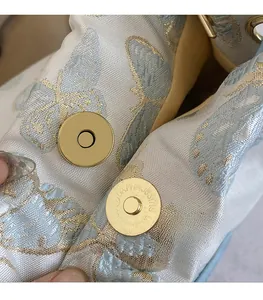 Détail de la boucle magnétique dorée et du tissu jacquard papillon bleu d'un sac seau