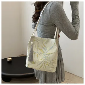 Detail of blue bamboo leaf embroidery on beige canvas tote bag with silk tassel accent