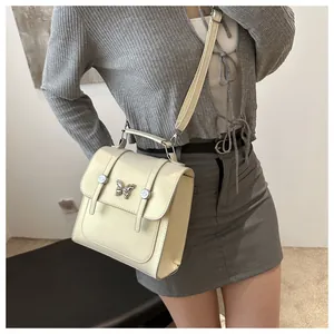 Detail of cream crossbody bag with silver butterfly buckle shown on a model