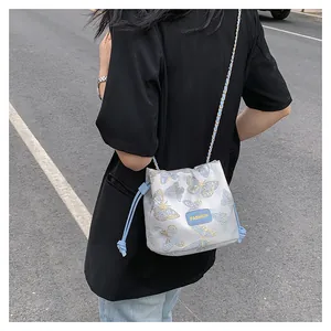 Détail du sac seau à cordon avec broderie papillon bleue et bandoulière en chaîne