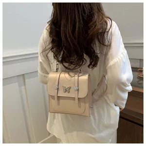 Detail of a beige mini backpack showing metal butterfly accent and magnetic buckle straps