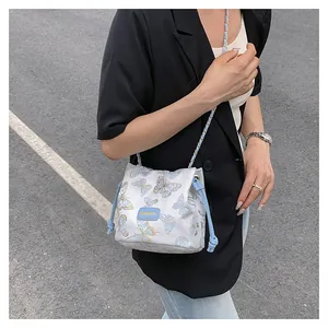 Détail du sac seau en tissu blanc avec broderies papillon bleues et chaîne en métal