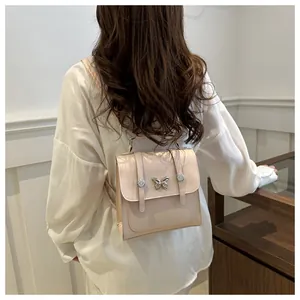 Detail of a beige faux leather backpack with silver butterfly ornament and buckle straps