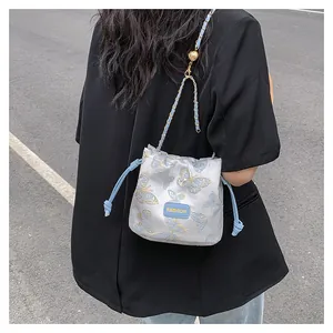 Détail du sac seau bleu clair à cordon avec broderie papillon et bandoulière chaîne