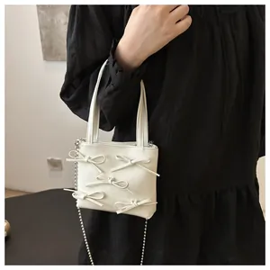 Close-up of a white leather mini bag with 3D bow accents and a silver bead chain strap