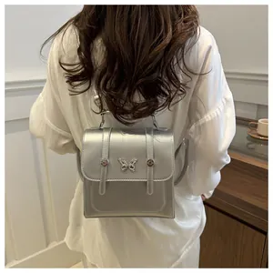 Rear view of a model wearing a metallic silver mini backpack with butterfly hardware
