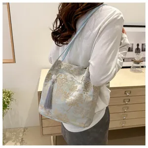 Detail of light blue jacquard shoulder bag with golden embroidery and grey tassel