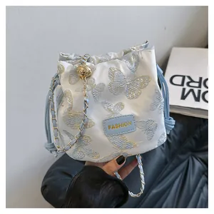 Détail du sac seau bleu clair avec broderie papillon et bandoulière en chaîne dorée