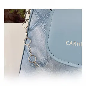 Detail of light blue denim texture and leather stitching on shoulder bag with CARHE logo