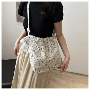 Dettaglio della borsa a tracolla beige a fiori con fiocco in pizzo indossata dal modello