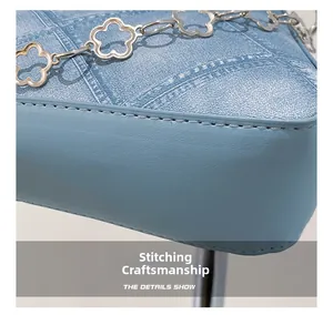 Detailed close-up of fine stitching on a blue denim texture shoulder bag with floral chain