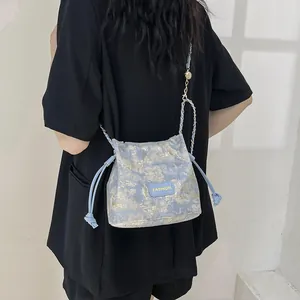 Sac seau jacquard bleu et doré avec bandoulière chaîne porté par un mannequin chic