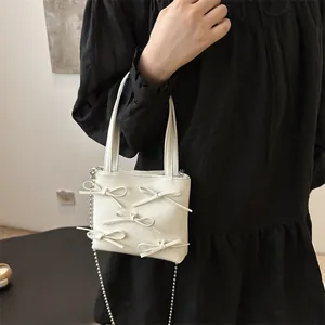 Mini cream tote bag with bows and silver chain strap shown on a black dress