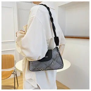 Detail of a patchwork denim underarm bag with woven strap and floral metal chain charm