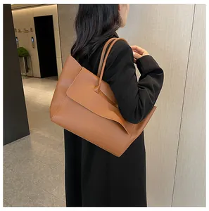Brown leather tote bag featuring a unique asymmetrical overlapping flap and slim shoulder straps