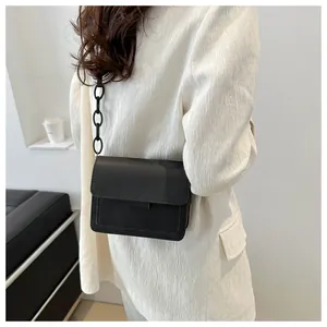 Dettaglio borsa a tracolla nera minimalista con catena opaca spessa su blazer bianco
