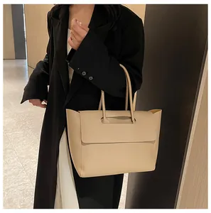 Close-up of minimalist beige leather tote bag held by a model in indoor setting