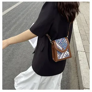Detail of a brown leather and blue woven fabric crossbody bag worn with a black suit