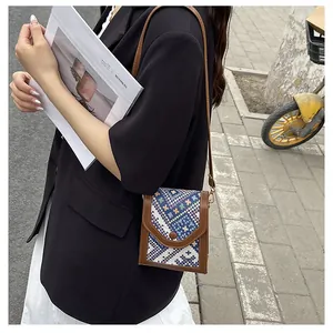 Detail of a woven patterned crossbody phone bag with premium brown leather trim and strap