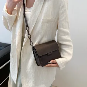 Piccola borsa a tracolla retrò marrone scuro con catena mostrata su modella in blazer bianco