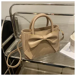 Close-up of beige handbag featuring a large bow decoration and gold metal hardware