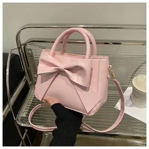 Detailed close-up of pink leather handbag featuring a large bow and gold hardware on a chair