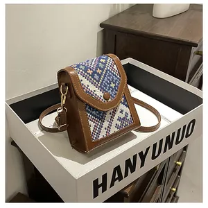 Detail view of a vintage geometric woven crossbody bag with brown leather trim and golden hardware