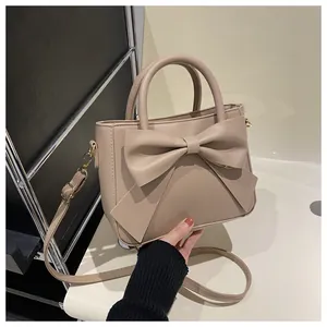 Close-up of elegant bow detail on beige rectangular handbag with golden metal hardware