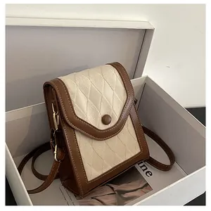 Detail of quilted fabric and brown leather trim on a square crossbody bag inside a white box