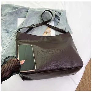 Deep brown pebble grain tote bag size comparison with a smartphone on blue denim