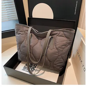 Detail of grey quilted down tote bag with wave stitching and dual handles in studio setting