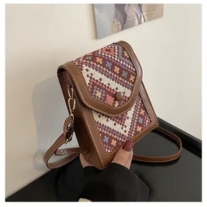 Detail of colorful geometric woven pattern and brown leather trim on a crossbody bag