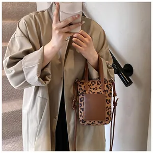 Detailed view of leopard print crossbody bag styled with a khaki trench coat indoors