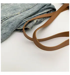 Dettaglio della borsa tote in denim azzurro con tracolla in pelle marrone e cuciture rinforzate